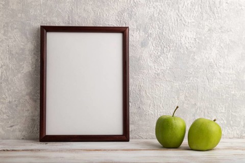 Brown wooden frame mockup with green apple on gray concrete background. Blank, vertical