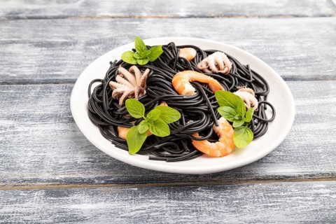 Black cuttlefish ink pasta with shrimps or prawns and small octopuses on gray wooden background.