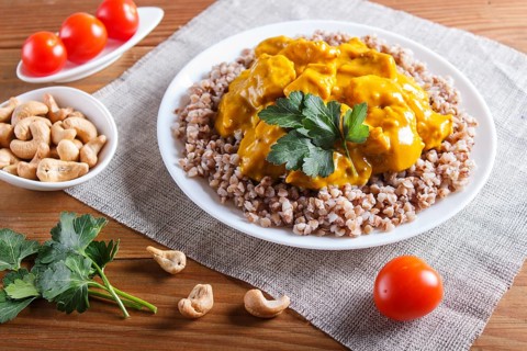 Buckwheat with chicken curry sauce with cashew on brown wooden background. close up