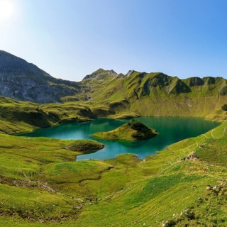 Schrecksee in the midst of green mountains under a clear sky, surrounded by lush vegetation and a