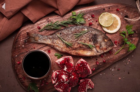 Gebratener Doradenfisch, mit Gewürzen und Kräutern, auf einem Holzbrett, Granatapfelsauce,