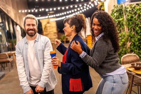 Multi-ethnic happy friends dancing while singing karaoke in the terrace of a bar