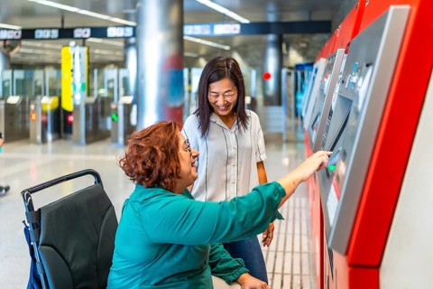 Disabled woman with wheelchair and chinese caregiver purchasing the ticket for the underground