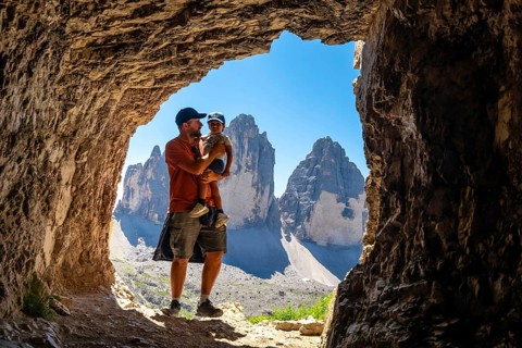 Father holding son admiring tre cime di lavaredo from inside a Tre Cime Cave during a trekking tour
