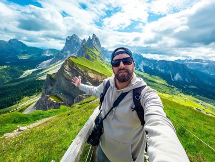 Photographer taking a selfie with outstretched arm, capturing the breathtaking seceda peaks and