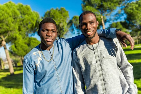 Two young senegalese men wearing traditional dashiki clothing embrace in a park, celebrating