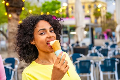 Close-up portrait of a latin woman biting an ice cream cone in the city
