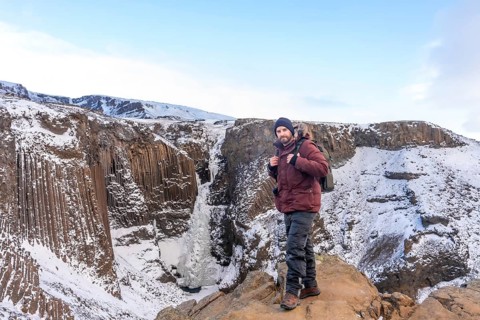 Portrait of a hiker at frozen Hengifoss waterfall in cold Iceland winter, volcanic cliffs