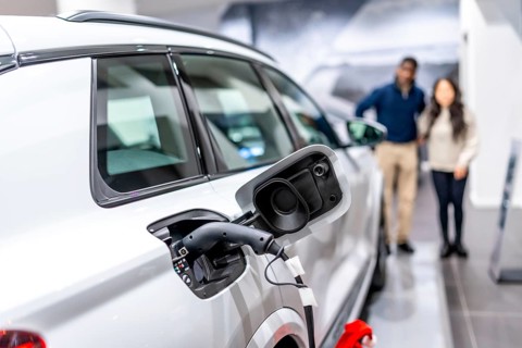 Couple looking at a charging electric car in a dealership, embracing sustainable transportation