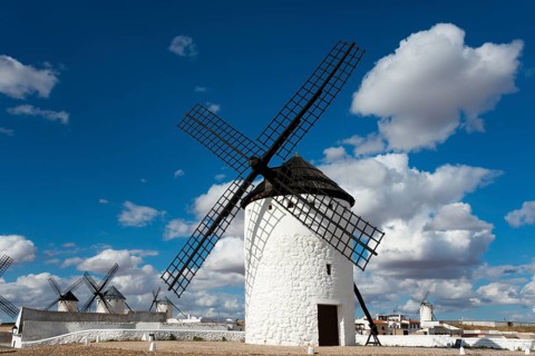 A historic white windmill against a blue sky with clouds and sunshine in a vast landscape,