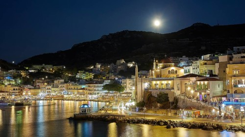 Illuminated coastal town at night with moon in the sky and water in the foreground, Rising full