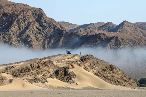 Safari vehicle on a hill in the Hoanib dry river, coastal fog, Kaokoveld, Kunene Region, Namibia,