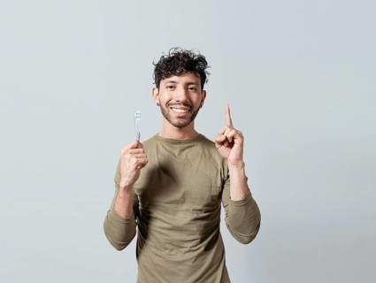 Smiling young man holding dental brush pointing up. Handsome guy holding toothbrush pointing an