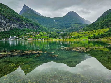 Mountainous landscape with a calm fjord reflecting the surrounding mountains and village,