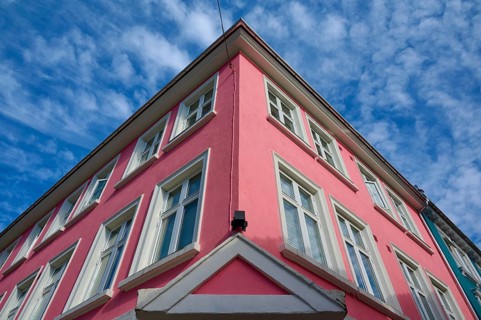 Historic building with pink facade and white window frames under a blue sky with light clouds,