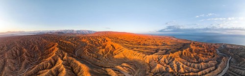 Panorama, landscape of eroded hills, badlands at sunrise, Issyk Kul Lake in the background, aerial