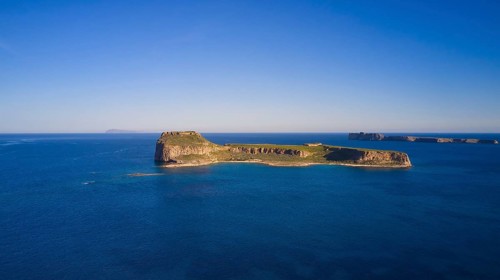 Drone shot, A deserted island in the vast blue ocean with rocky coastlines and clear skies,