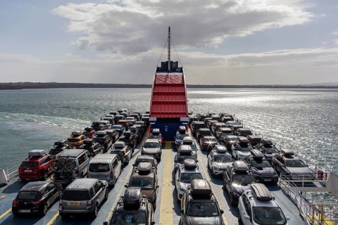 Ferry loaded with cars, sun reflected on the sea, bright sky in the background, Rosslare Harbour