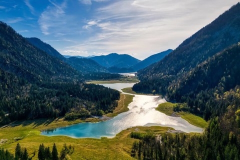 A quiet valley with a lake, surrounded by wooded mountains under a sunny sky, Mittersee