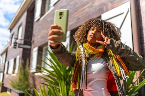 Beauty latin woman gesturing victory while taking a selfie standing next to a house