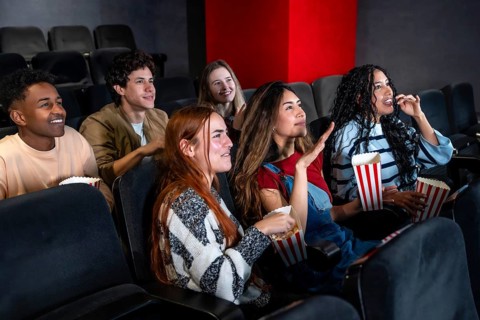 Friends enjoying a film in a movie theater, munching on popcorn and sharing laughter, creating