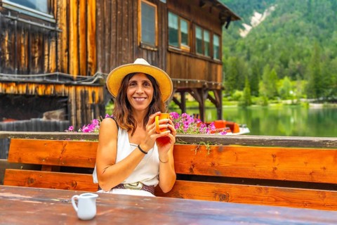 Woman with straw hat enjoying a hot drink in a bar with mountain lake view in the dolomites