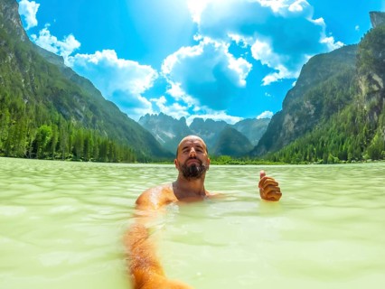 Tourist gesturing thumbs up while swimming in the turquoise water of lago di landro, surrounded by
