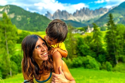 Mother carrying her son on her shoulders, enjoying a sunny day in the italian dolomites with the
