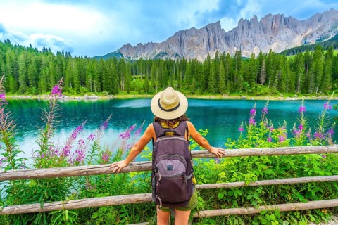 Female tourist with backpack admiring the stunning turquoise waters of lake carezza and the latemar