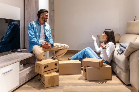 Young couple talking and smiling while unpacking cardboard boxes in new home, planning the