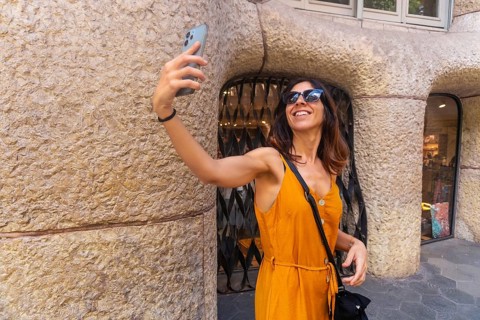 Smiling woman taking selfie with smartphone in front of casa mila in barcelona, enjoying summer