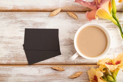Black paper business card mockup with orange day-lily flower and cup of coffee on white wooden