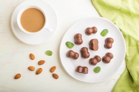 Chocolate candies with almonds and a cup of coffee on a white wooden background and green textile.