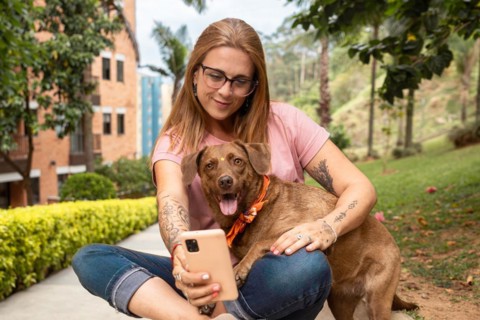 Woman sitting with reading glasses taking a selfie with her pet sitting in the park