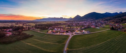 Panoramic view of a village in a wide green plain with mountains in the background at dusk, Bad