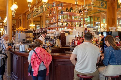 Cosy café with people at the counter, warm wood panelling and glowing lamps, Paris