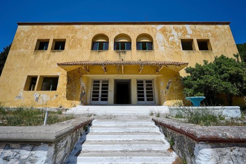 An abandoned building with a crumbling façade and an external staircase on a sunny day under a blue