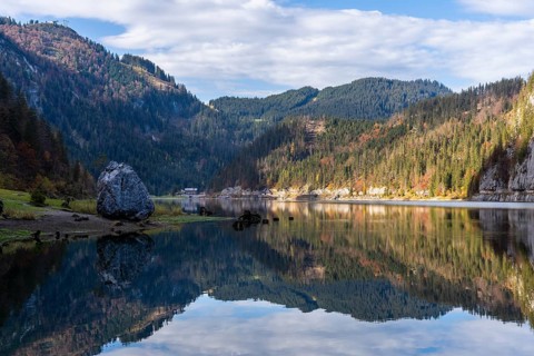 The Vordere Gosausee in autumn with a view of the Gasthof Gosausee. On the left a large rock on the