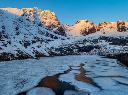 Aerial view of icy lake in front of steep mountains, winter, sunrise, Storvatnet, Flakstadoya,
