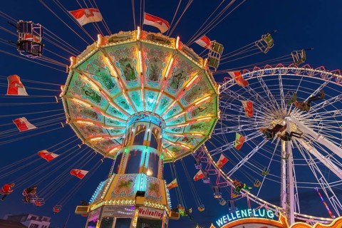 A funfair at dusk with illuminated chain carousel and Ferris wheel, Europa Rad, rides, wave flight,