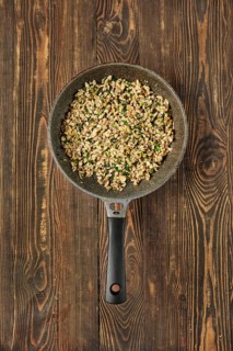 A skillet filled with sauteed diced mushrooms mixed with fresh herbs on a rustic wooden table. The