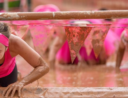Participant climbs through muddy obstacles in a sporting competition