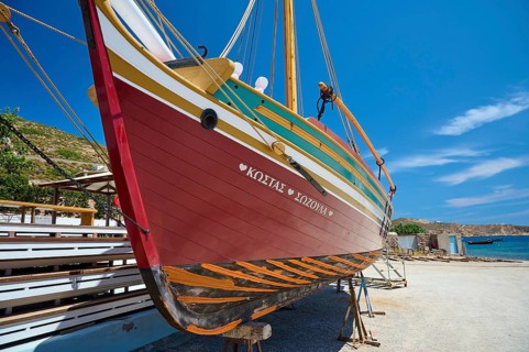 A colourful wooden boat hangs in a dry dock under a clear blue sky and calm atmosphere, Patmos