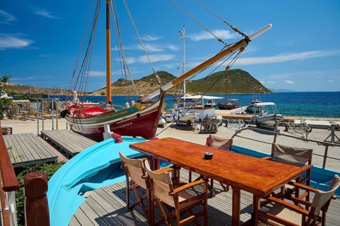 A harbour scene with wooden boats and a table with chairs and a blue boat in the foreground in