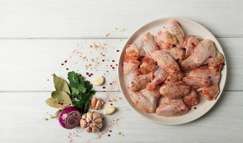 Frische, rohe Hähnchenflügel, mit Gewürzen, auf einem weißen Holztisch