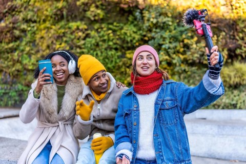 Three young content creators are filming a video blog outdoors in a winter city setting, using a