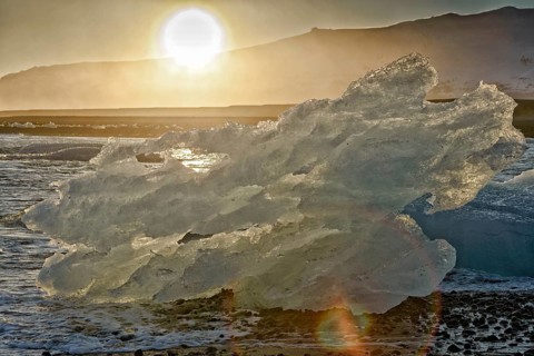 Backlit block of ice, beach at glacier lagoon Jökulsarlon, Breiðamerkursandur, south coast,