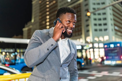 Young businessman smiling while talking on his smartphone in a bustling city street at night,