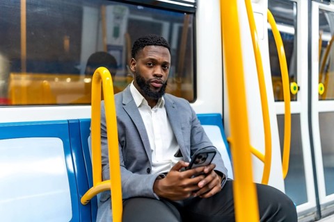 Young businessman sitting on a subway train, using a smartphone during his daily commute, staying