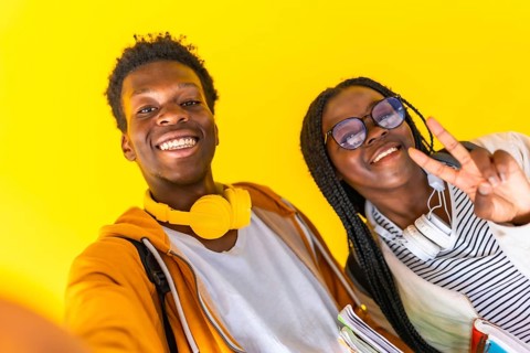 Studio portrait with yellow background of African students taking selfie and gesturing success with